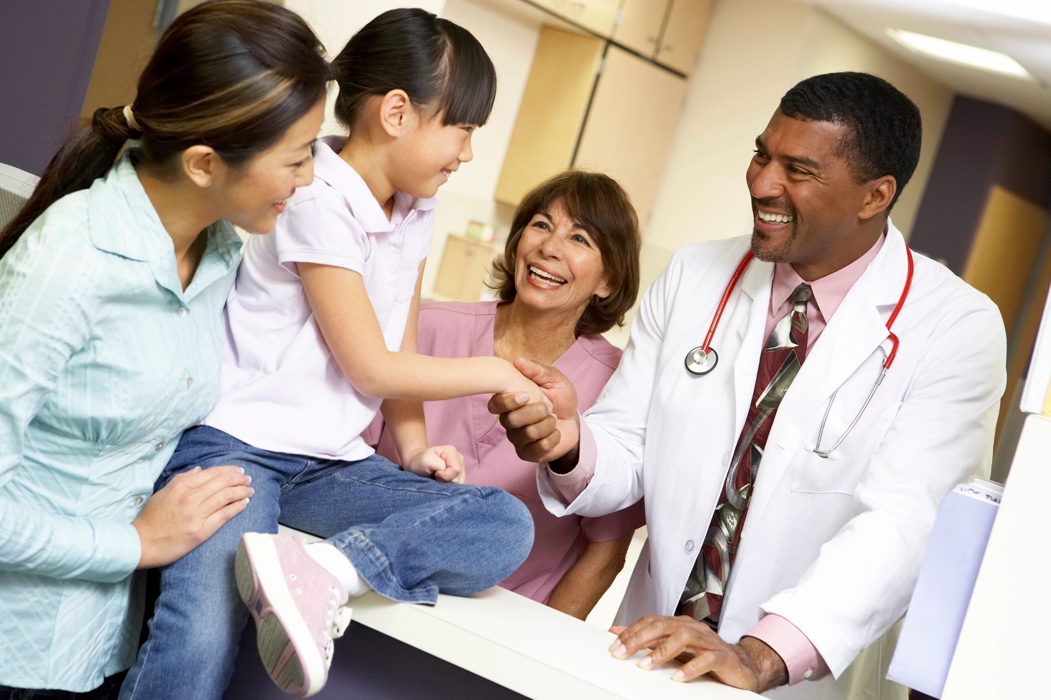 Family at nursing station talking to healthcare workers including doctor shaking patient's hand.