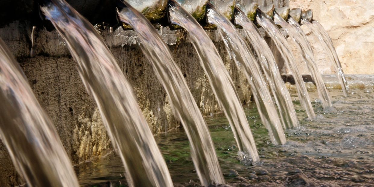 Multiple water streams flowing from spouts into a pool.