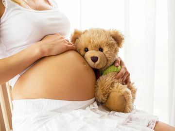 Pregnant woman holding a teddy bear against her belly.