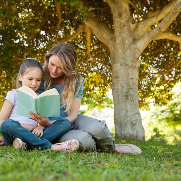 A mother and a daughter sitting under a tree and reading a book