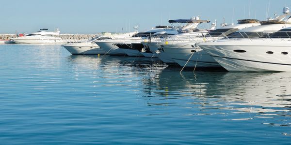 A row of white yachts docked in calm blue water under a clear sky.