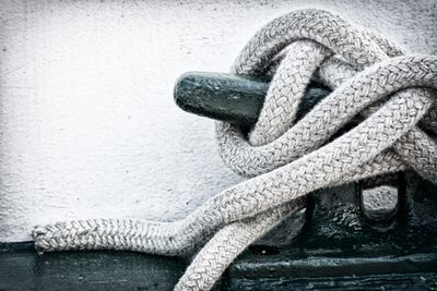 Close-up of a white rope tightly knotted around a metal cleat on a boat.
