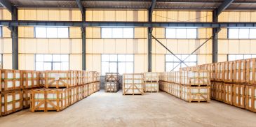 Spacious warehouse with neatly stacked wooden crates and large windows.
