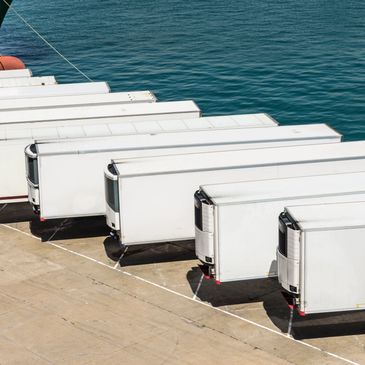 A row of white refrigerated trailers parked by the water.