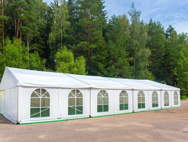 Large white event tent set up on a paved surface near a forest.