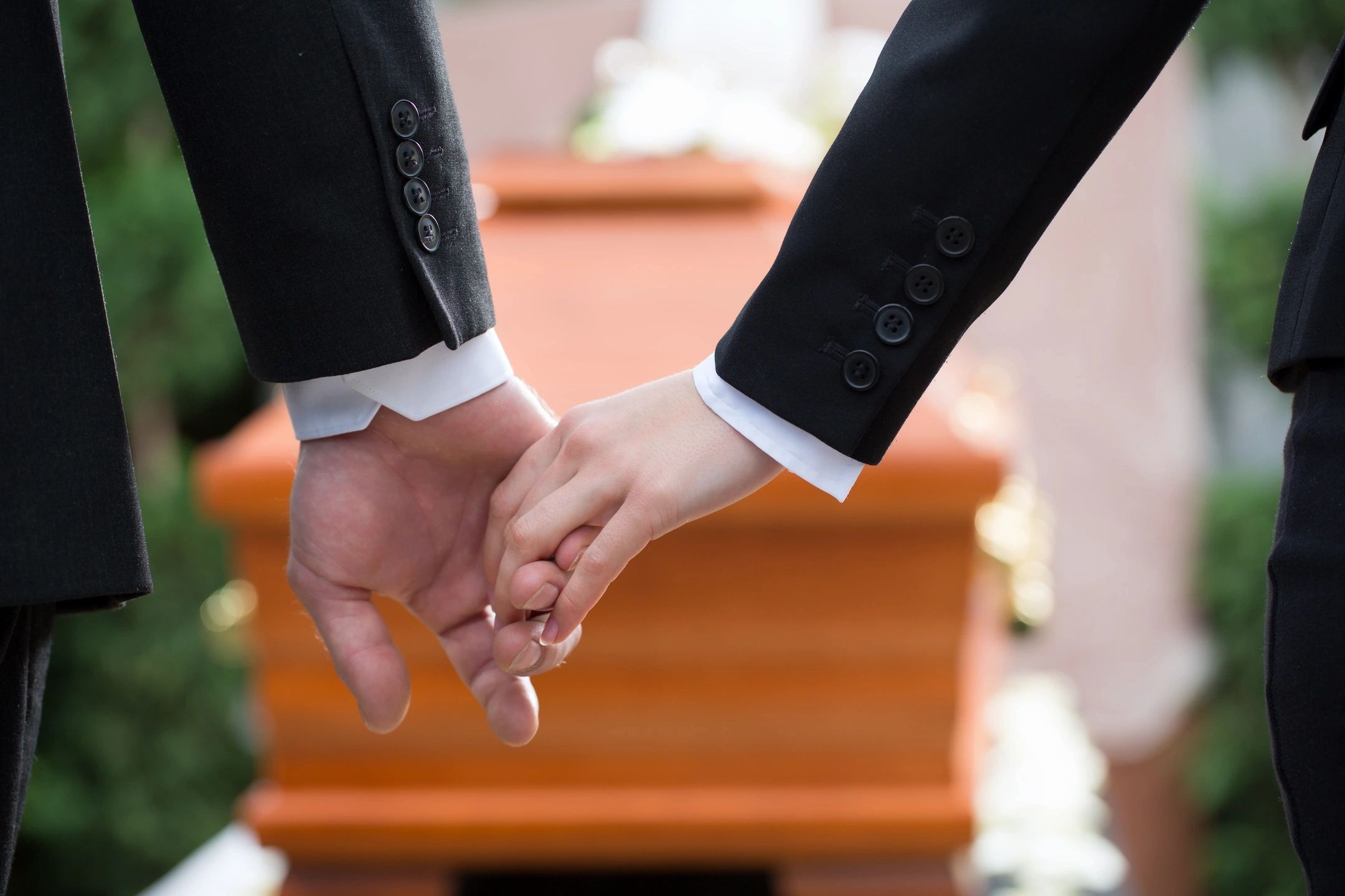 Two people holding hands with a wooden coffin in the background
