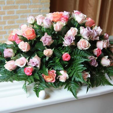 Bouquet of pastel-colored roses with green leaves on a white surface.