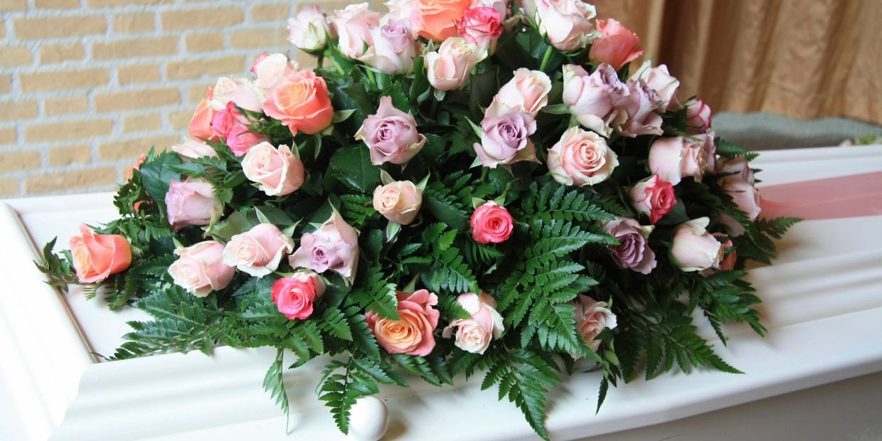 A floral arrangement of pastel roses on a white coffin.