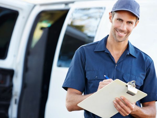 Smiling delivery man holding clipboard in front of a white van.