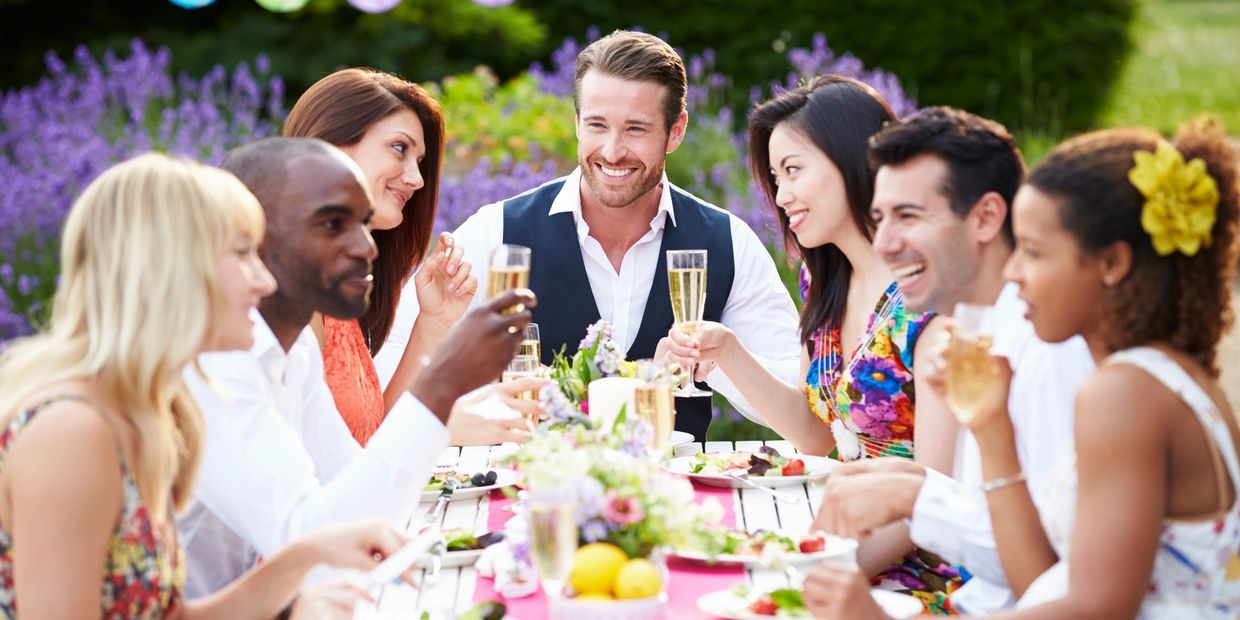 Friends enjoying a cheerful outdoor meal with drinks and smiles around a decorated table.
