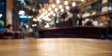 Empty wooden table in a cozy, warmly lit cafe with blurred background.