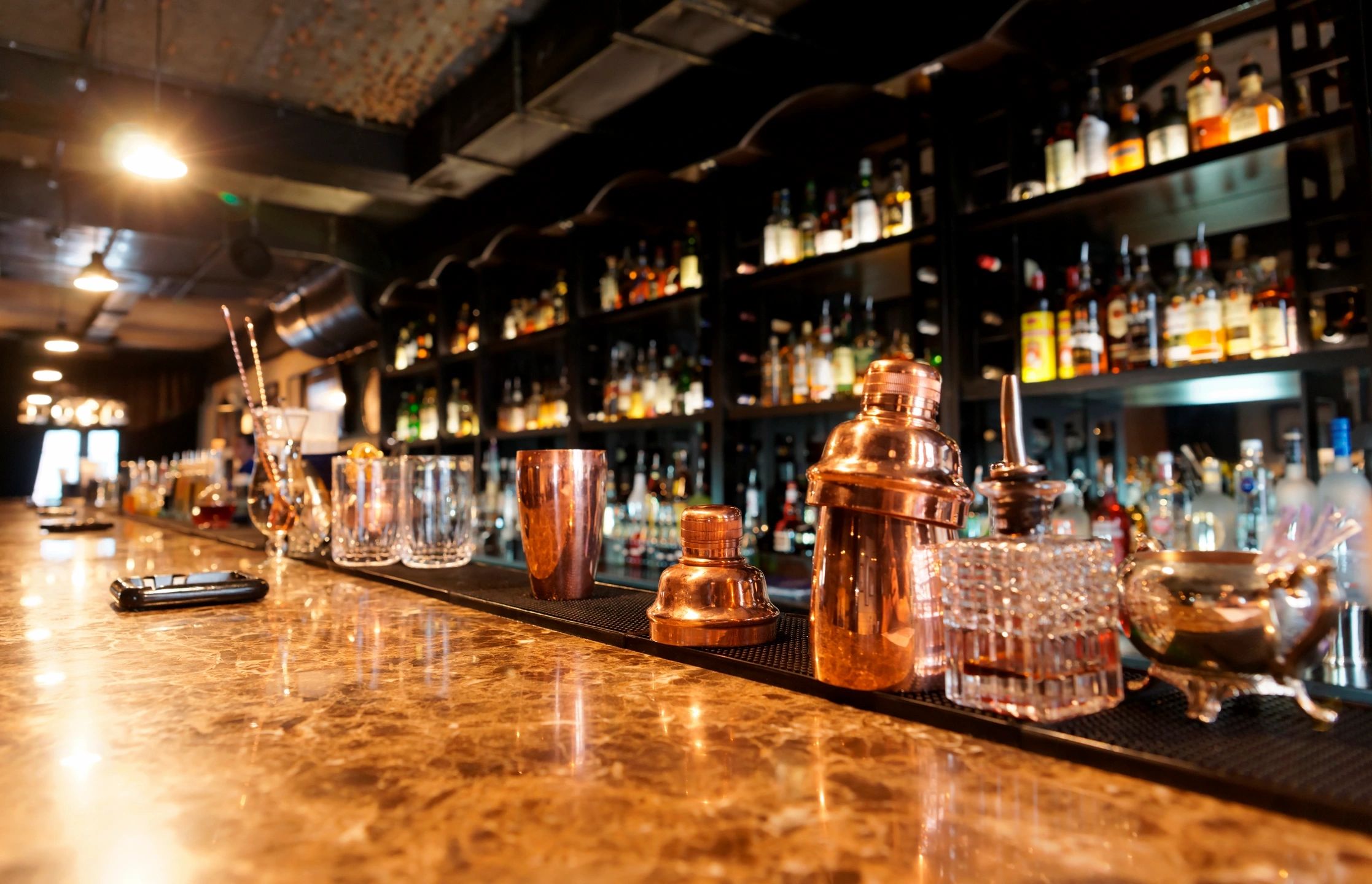 Copper barware and glasses lined up on a polished marble bar counter.