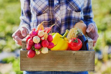 Person holding a wooden crate full of fresh vegetables.