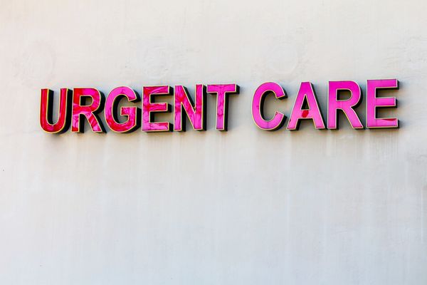 Bright pink 'URGENT CARE' sign on a plain wall.