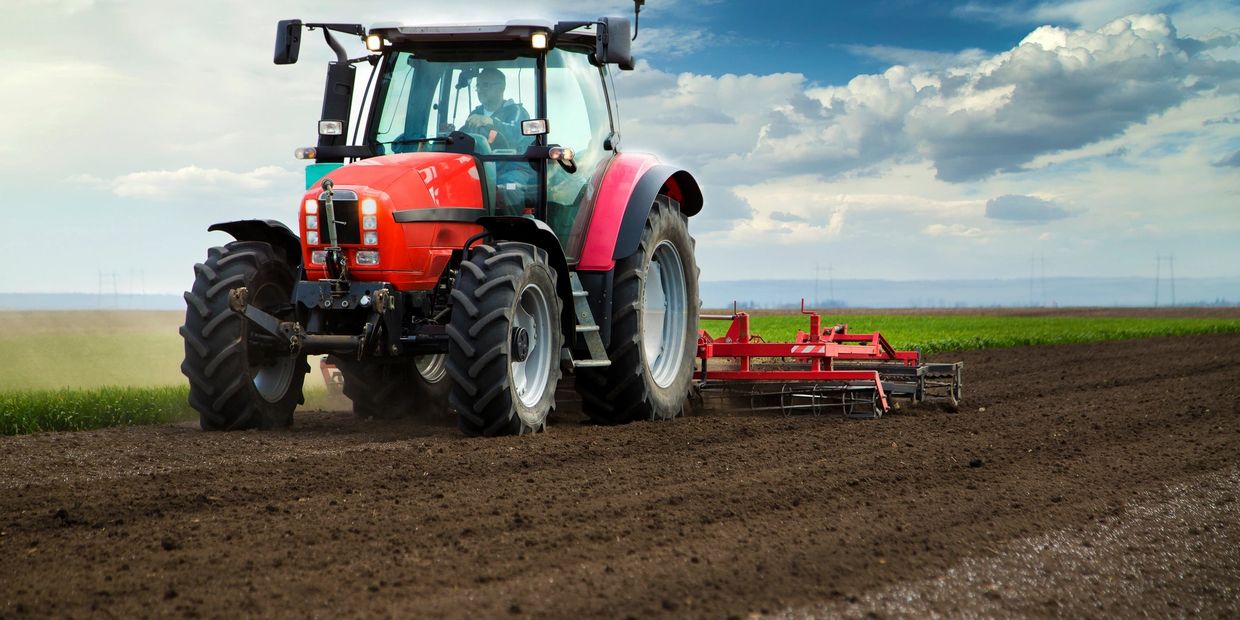 Red tractor tilling soil on a farm under a cloudy sky.