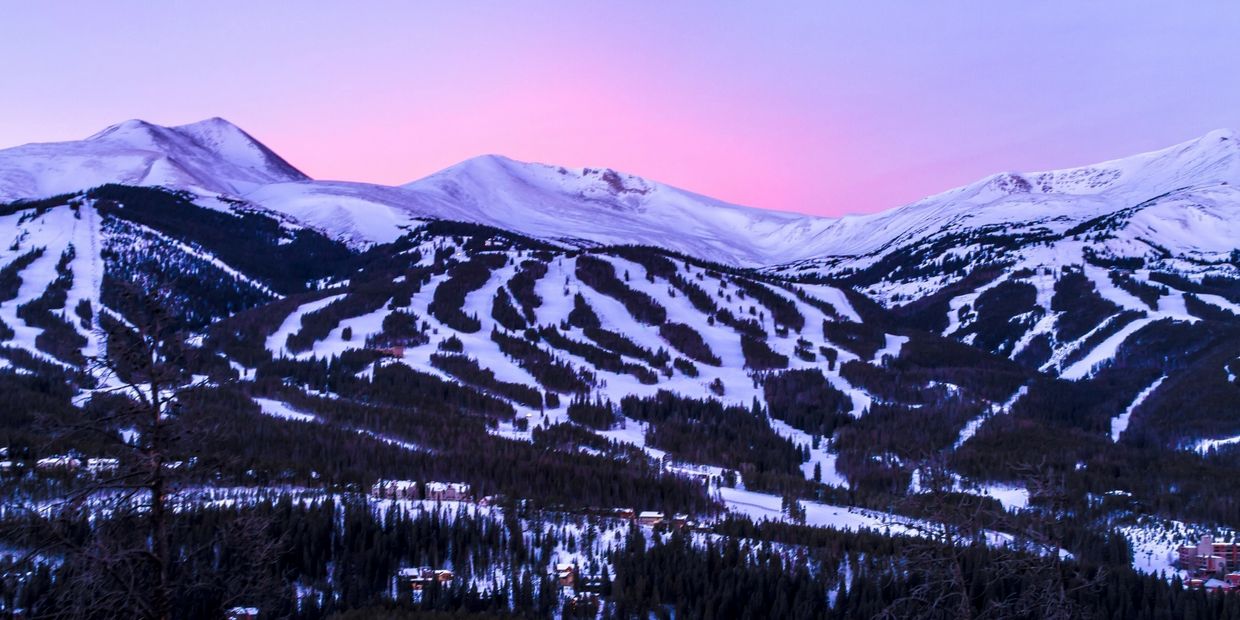 Mountain town with sunset behind snow covered ski slopes.