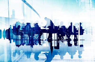 Silhouettes of business people in a modern glass office with cityscape reflections.