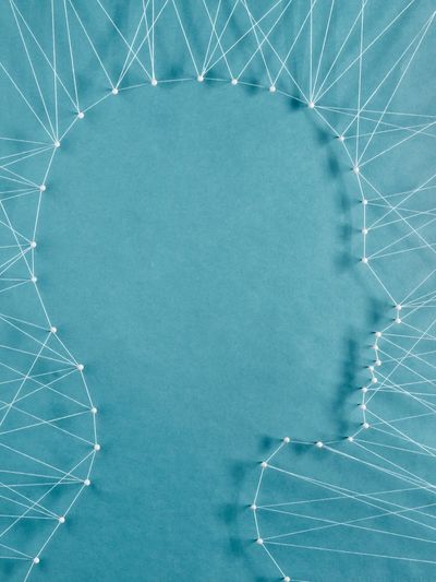 The shape of a profile human head, formed by threads and nodes, pulled against a blue background