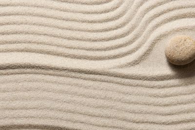 Two zen rocks in the warm sun sitting on smooth sand, surrounded by ripples carved into the sand.