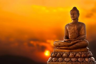 A serene Buddha statue against a vibrant sunset sky.