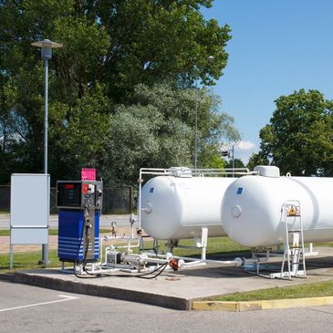 Outdoor fuel station with white storage tanks and fueling pump under clear sky.