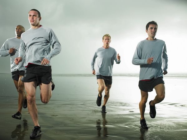 Four men running on a wet beach in matching gray shirts and black shorts.