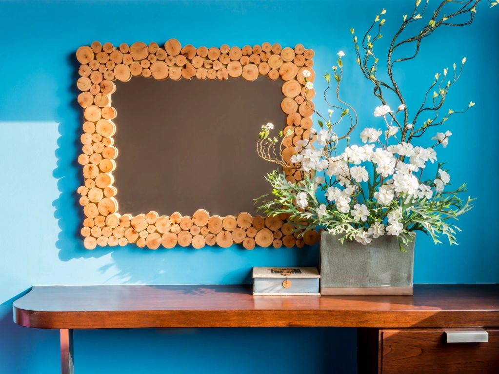 Decorative wooden framed mirror above a wooden desk with flowers.