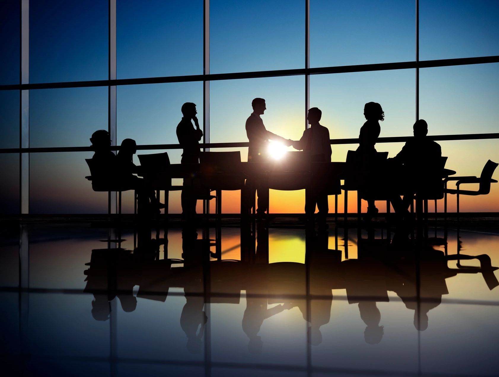 A board room with wall to wall windows, sun shining in and board members gathering and agreeing. 