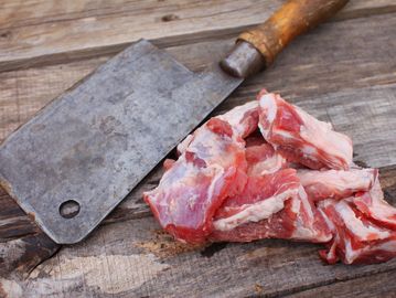 Raw meat pieces with a cleaver on wooden surface.