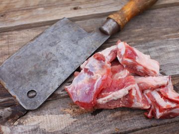 Raw meat pieces with a cleaver on wooden surface.