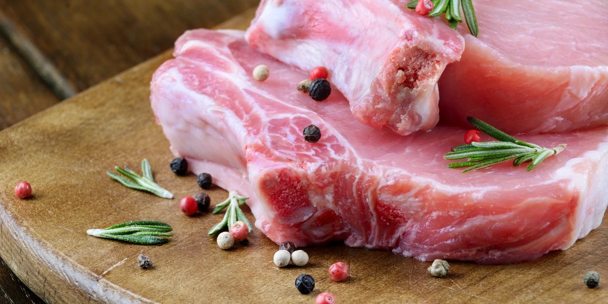 meat, pork chop, raw meat pictured with peppercorns and rosemary on a cutting board
