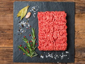 Raw ground meat with herbs and spices on a slate board.