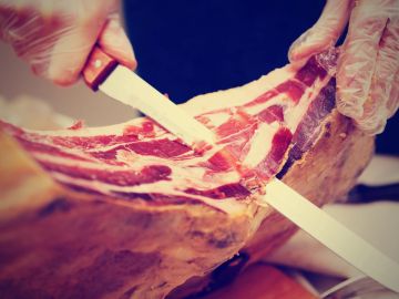 Carving thin slices from a large piece of cured meat.