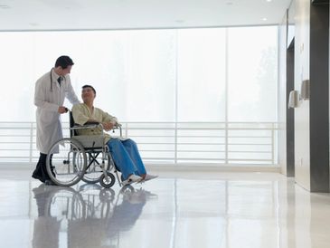 Doctor assisting patient in wheelchair in a hospital corridor.