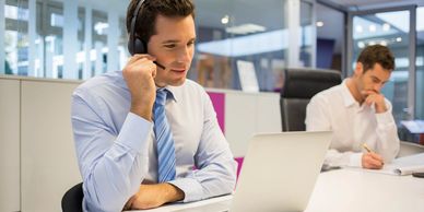 Man in headset working on laptop in office.
