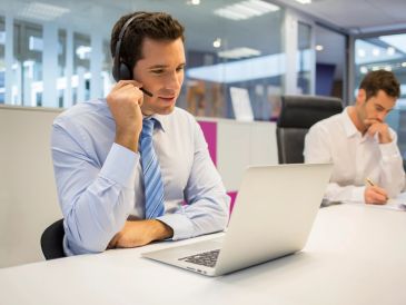 Man wearing headset working on laptop in office environment.