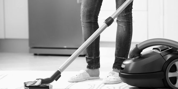Person vacuuming a rug with a canister vacuum cleaner in a kitchen.
