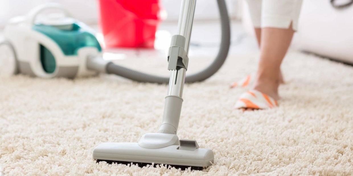 Person vacuuming a white shag carpet with a vacuum cleaner.