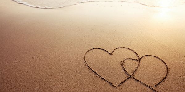 two connecting hearts drawn into sand on a beach with a bit of ocean water showing at the top of the