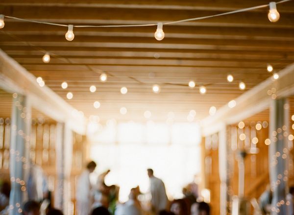 Blurry image of an event with string lights and people indoors.
