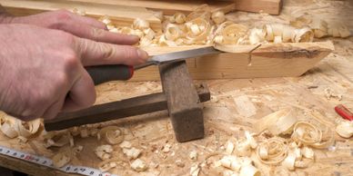 Close-up of hands carving wood with a chisel and wooden clamp on a workbench.