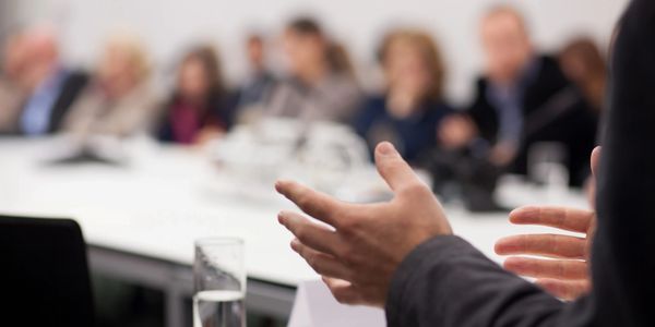 picture of a speakers hands as he addresses a seated audince