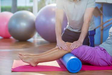 Therapist using a foam roller on a patient's leg during rehabilitation.