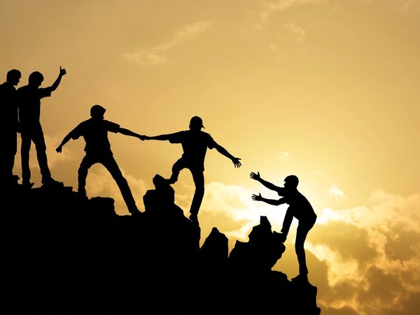 People helping each other climb a mountain