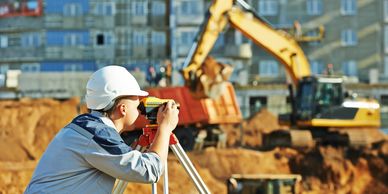 Construction worker using surveying equipment at a building site.