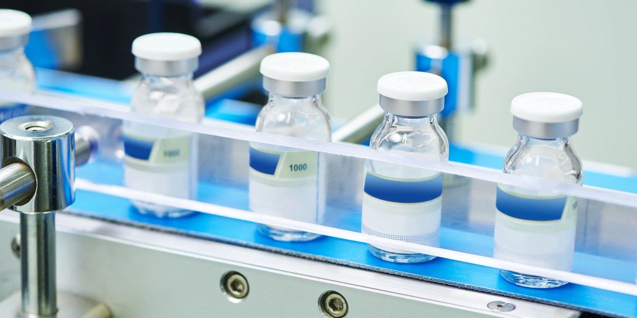 Glass vials with white caps on a conveyor belt in a pharmaceutical production line.