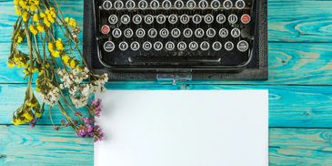 Vintage typewriter, flowers, and blank paper on turquoise wood.