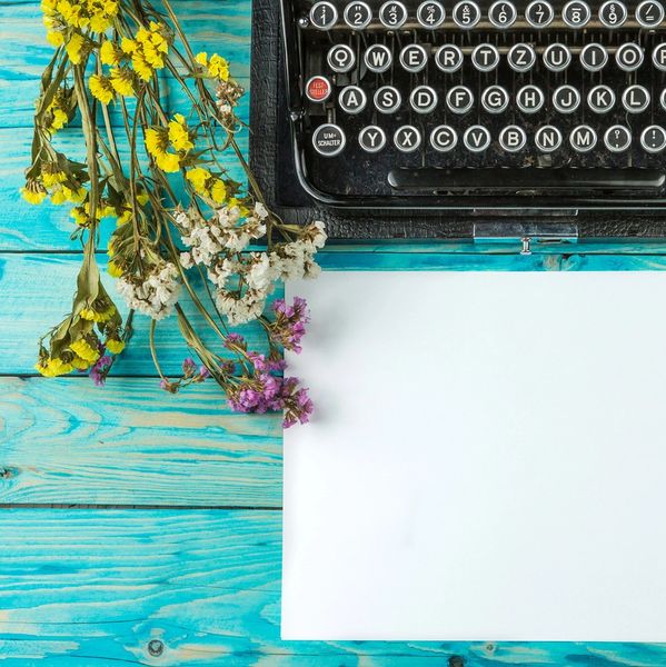 Vintage typewriter with flowers and blank paper on turquoise wooden table.