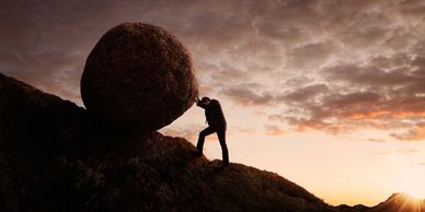 Man pushing massive boulder stone up a hill