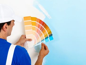Painter choosing paint colors from a fan deck against a blue wall.